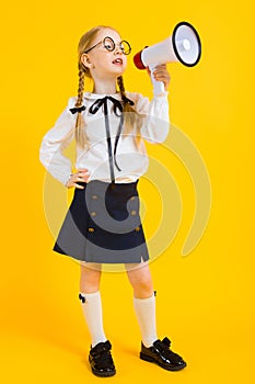 Girl with red pigtails on a yellow background. A charming girl in round transparent glasses screams into the loudspeaker