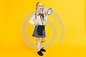 Girl with red pigtails on a yellow background. A charming girl in round transparent glasses screams into the loudspeaker