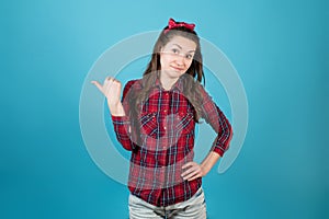 Girl in a red plaid shirt smiles skeptically and points a finger to the side
