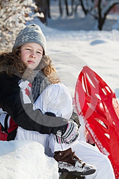 Girl with red plastic sled in a snowy park