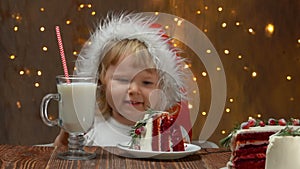 Girl in red Santa Claus Hat is rubbing her eyes and then eating red velvet cake