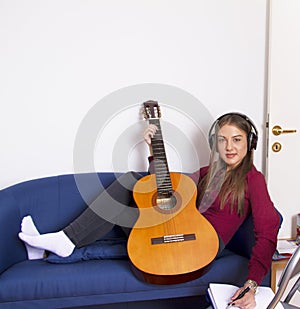 A girl in a red shirt Holds a guitar and listens to music and writes a song in a note book..