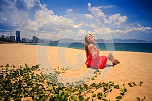 girl in red sits on sand looks at sea on foreground creepers