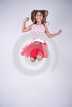 Girl with red skirt jumping happy and smiling with hands up and hair in the wind