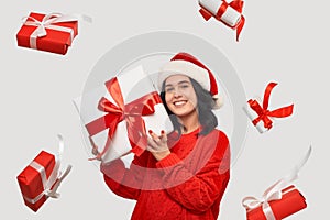 Girl in a red sweater and Santa Claus hat holding white giftbox with red ribbon