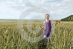 Girl with red tulip flowers posing in the wheat field, bright sun, beautiful summer landscape