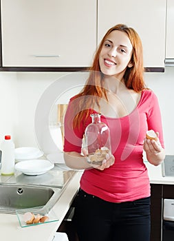 Girl in red washing bottle with egg shell in kitchen