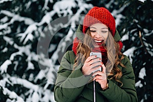 Girl in red winter hat and scarf using smartphone and smiling.