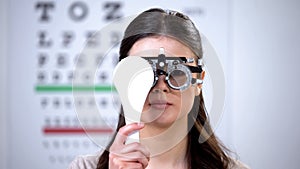 Girl in refractor closing one eye, ophthalmologist appointment, vision check-up