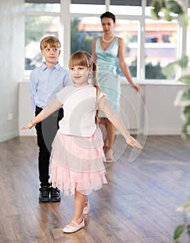 Girl rehearsing elegant curtsy with boy dance partner and female teacher