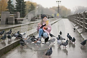 Girl rejoices and feeds pigeons in city park in autumn rainy weather