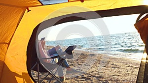 Girl relaxing in a chair on sandy beach near the hiking tent