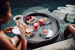 Girl relaxing and eating fruits in the pool on luxury villa in Bali. Exotic summer diet. Tropical beach lifestyle