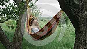 Girl relaxing in hammock with apple at green garden. young female in hat enjoying vacation outdoors lying in hammock at countrysid