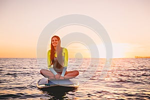 Girl relaxing on stand up paddle board, on a quiet sea with warm sunset colors.