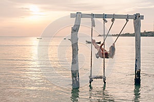 Girl relaxing in swings on sunset beach