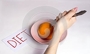 The girl reluctantly sits on a fruit diet, poking an orange with a fork