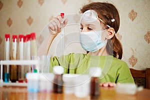 Girl in respirator attentively looks at test tube