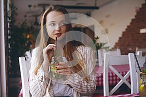 The girl in a restaurant on the ship near the river drinks mojito. Brunette smiles and drinks mojito in a glass jar. Girl with lon