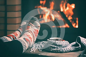 Girl resting and warming her feet by a burning fireplace in a country house on a winter evening. Selective focus.