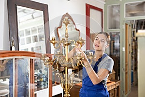 Girl restorer with brush removes dirt and dust deposits from bedside antique floor lamp