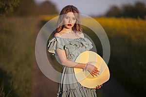 Girl in retro clothes with a straw hat stands on a background of a yellow field.