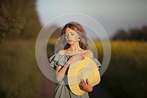 Girl in retro clothes with a straw hat stands on a background of a yellow field.