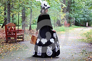 Girl in retro dress 18th century with valise in park