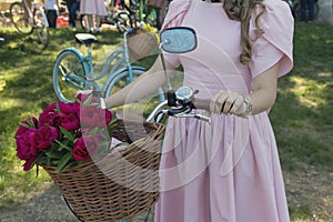 Girl in retro dress with a basket of flowers on the bike