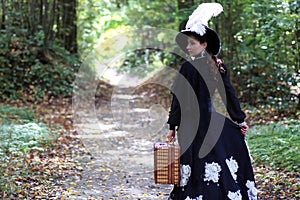 Girl in retro dress 18th century with valise in park