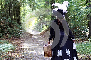 Girl in retro dress 18th century with valise in park