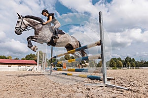 Girl rider on dapple gray horse jumping over a hurdle