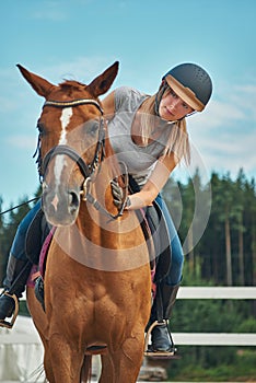 Girl rider in helmet stroking horse sitting astride