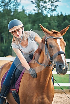 Girl rider in helmet stroking horse sitting astride