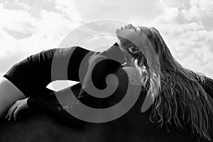 Girl rider lies bent on a horse in the field. Fashion portrait of a woman and the mares are horses in the village in the sky