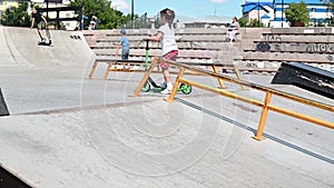 A girl rides a 2-wheeled scooter on the sports slides in the park in the early summer morning. co