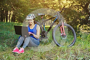 girl rides a biker after a trip to the pine forest and makes a further route on the laptop.