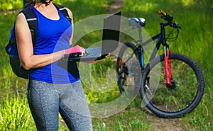 Girl rides a biker after a trip to the pine forest and makes a further route on the laptop.