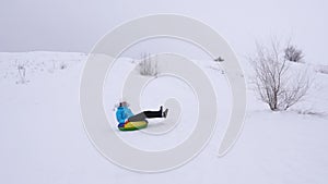 Girl rides from high mountain on snow saucer over snow in winter and laughs with pleasure. Cheerful woman sledding