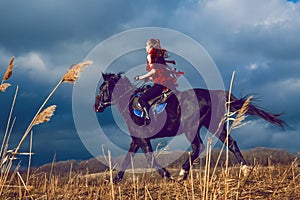 Girl rides on a horse in red dress developing in the field on sky