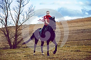 Girl rides on a horse in red dress developing in the field on sky