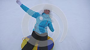 Girl rides snowy road on snow saucer over snow in winter and laughs with pleasure. Cheerful woman on sled. Christmas