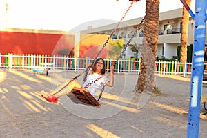 The girl rides on a swing in the playground.