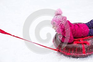 A girl rides a tube from a slide in winter in a snowfall. Tubing, winter sports outdoor and family entertainment. Warm clothes,