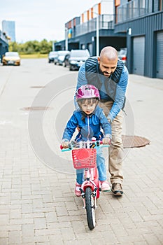 Girl riding a bike with her father\'s hepl. Family outdoors activities together
