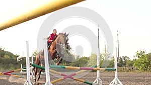 Girl riding a brown horse jumps over the barrier.