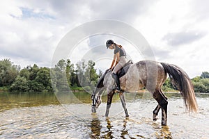 Girl riding gray horse down the calm river water