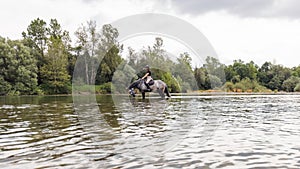 Girl riding gray horse down the calm river water