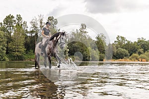 Girl riding gray horse down the calm river water