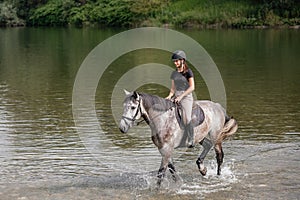 Girl riding gray horse down the calm river water